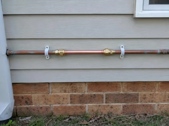 Repaired copper water pipe on exterior wall above brick base in Coal Point