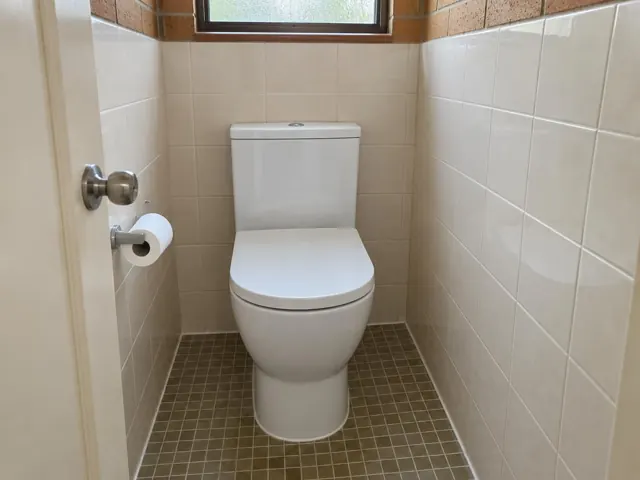 White toilet in a small tiled bathroom with window and tiled floor in Rathmines